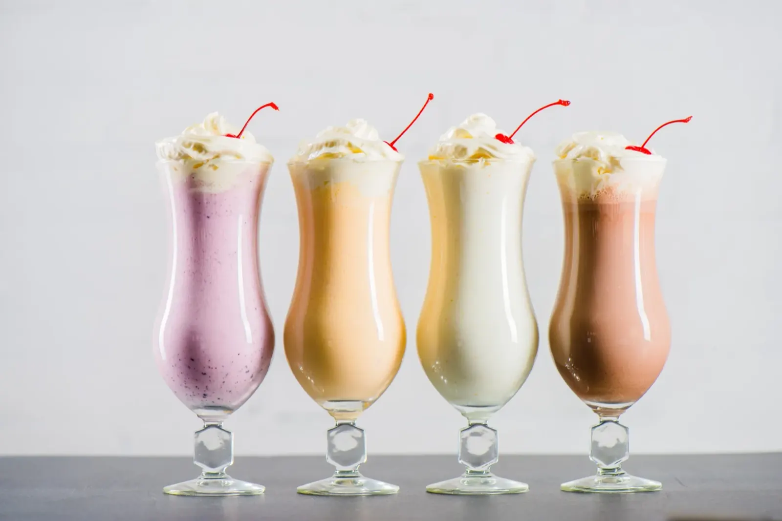Vier Milchshakes in Gläsern mit Sahnehaube und Kirsche